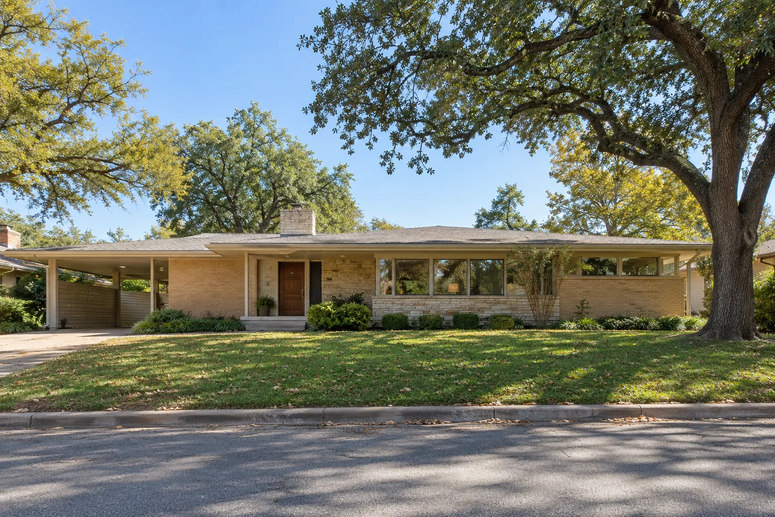 Mid-century ranch home with a low-pitched roof under mature trees in Dallas, TX